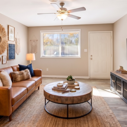 Bright, boho-inspired apartment living room featuring a cognac leather sofa, round wood coffee table, wall-mounted TV, and warm neutral décor.