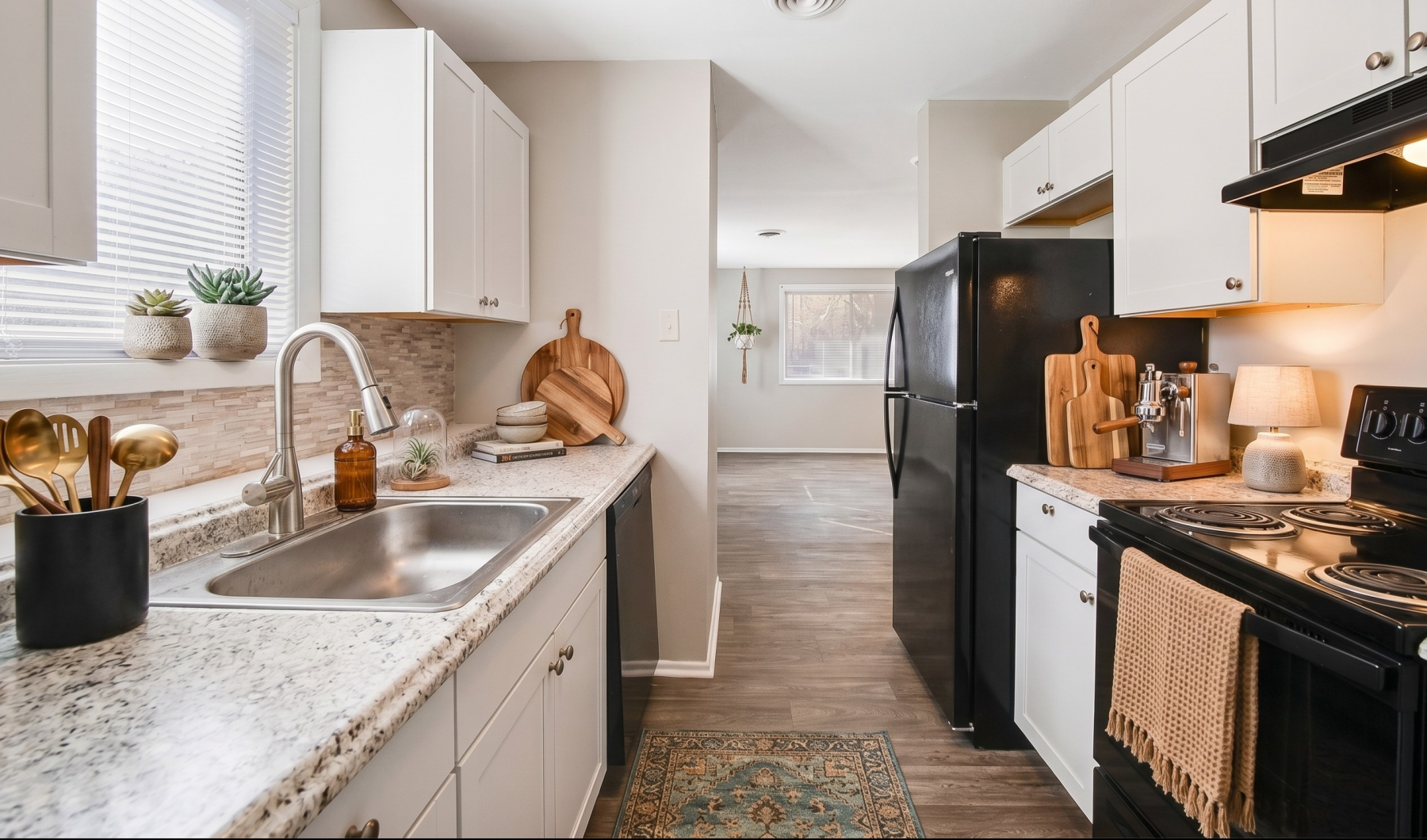 Updated apartment kitchen with white cabinetry, granite-style countertops, black appliances, a stainless-steel sink, and natural light from the window.