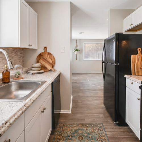 Updated apartment kitchen with white cabinetry, granite-style countertops, black appliances, a stainless-steel sink, and natural light from the window.